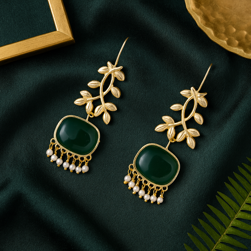 Gold earrings with green stones and pearl-like beads on a dark green fabric background