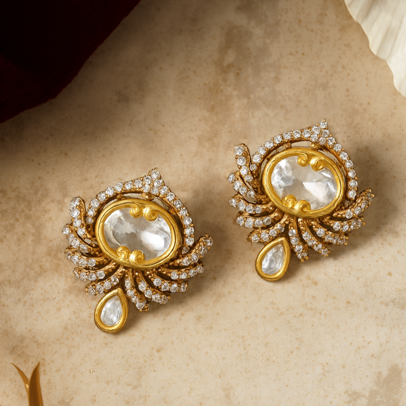 Gold earrings with pearl-like stones on a beige surface