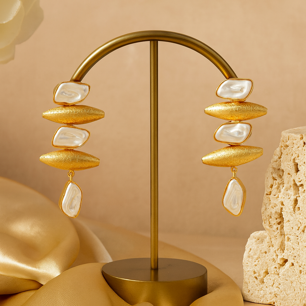 Gold and white earrings on a gold stand against a beige background