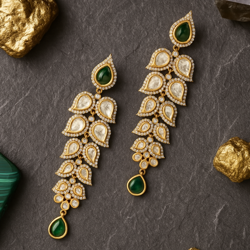Ornate gold and green earrings on a dark stone surface with gold and green stones.