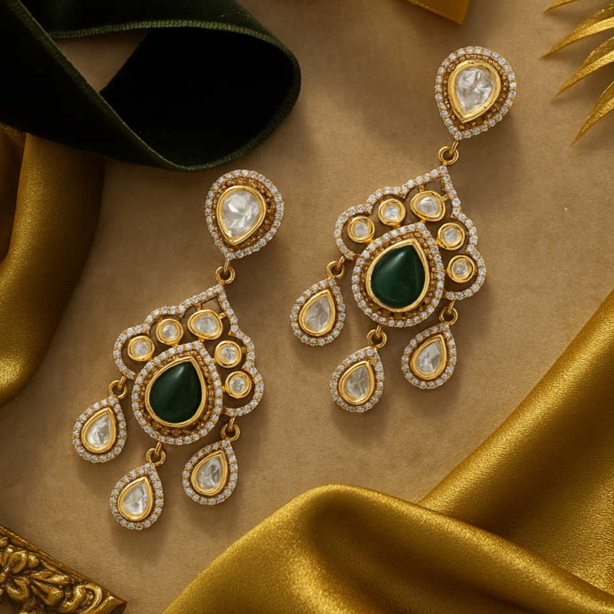 Ornate gold earrings with green gemstones on a gold fabric background