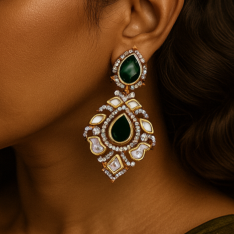 Woman wearing a pair of ornate earrings with green gemstones on a dark background