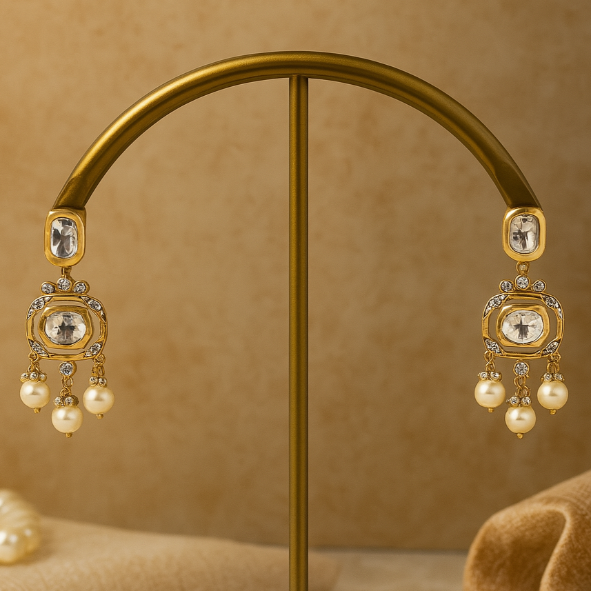 Gold earrings with pearls on a gold stand against a beige background