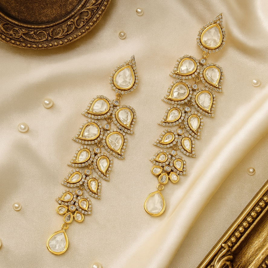 Gold earrings with teardrop-shaped gemstones on a beige fabric background