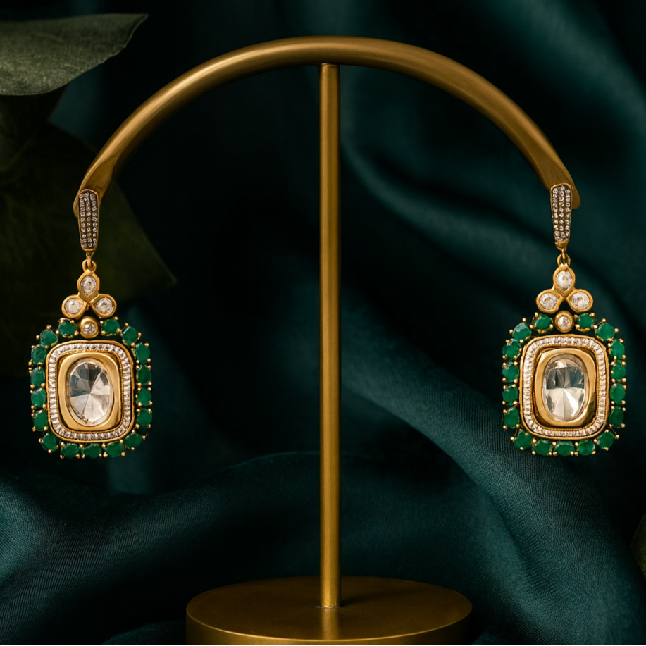 Gold earrings with green gemstones on a gold stand against a dark green fabric background