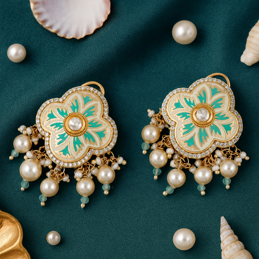 Decorative earrings with pearls and green accents on a teal fabric background