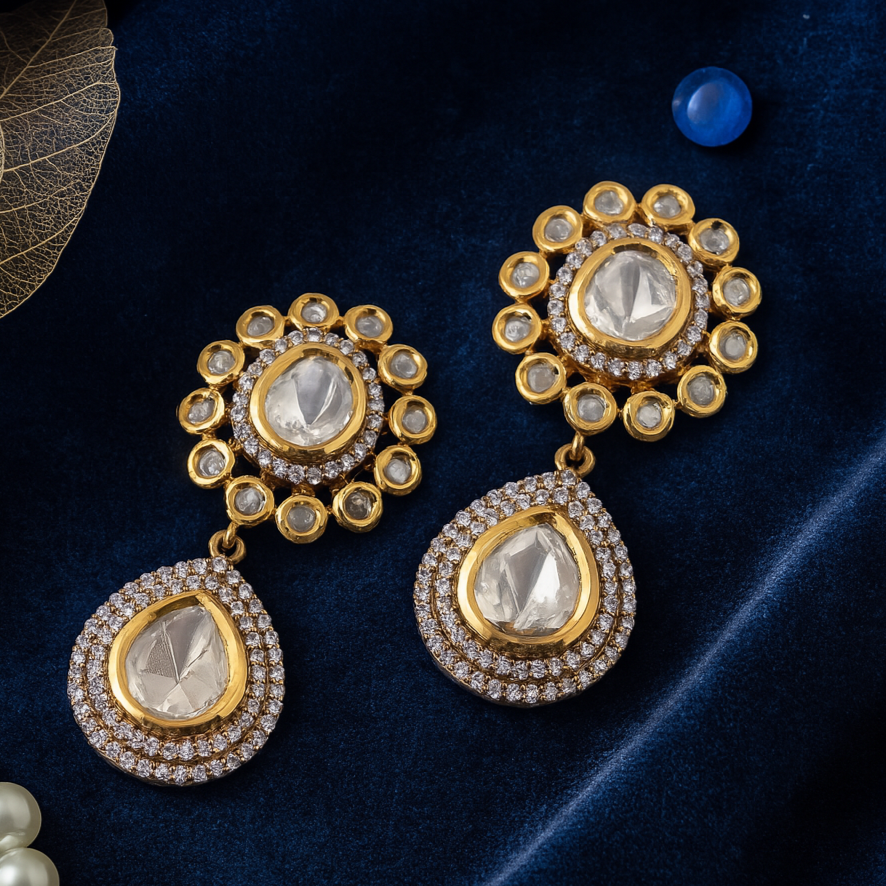 Gold earrings with clear gemstones on a dark blue fabric background