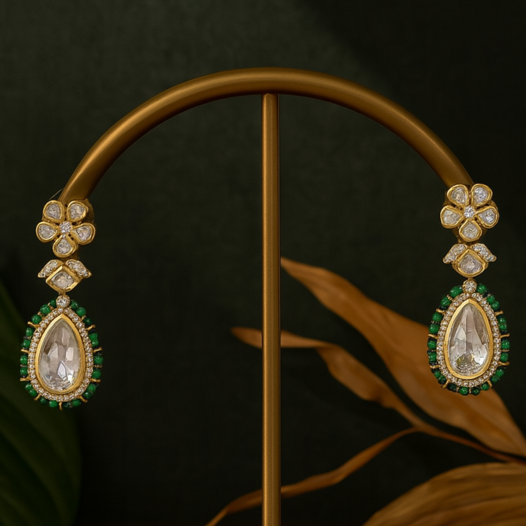 Gold earrings with green and clear stones on a dark background