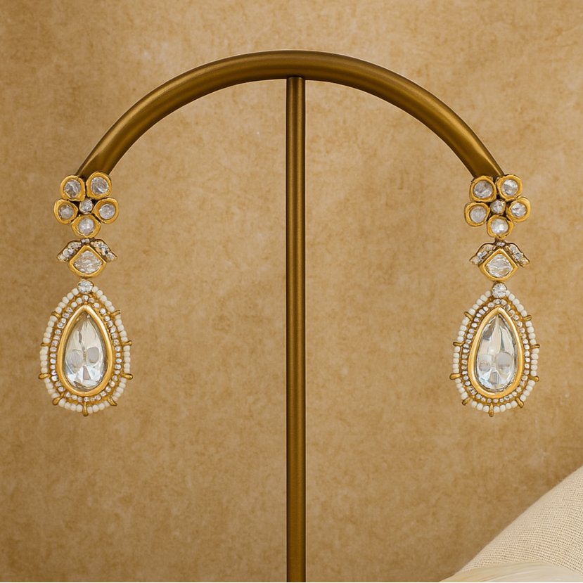 Gold earrings on a gold stand against a beige background