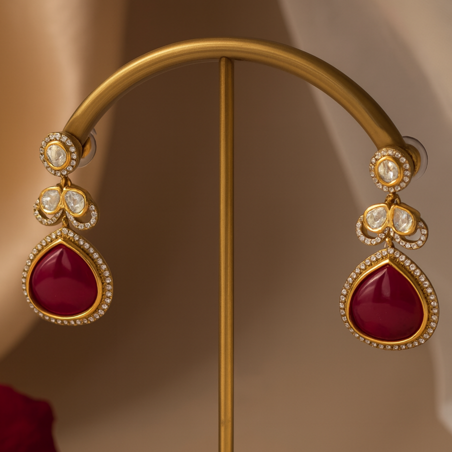 Gold earrings with red gemstones on a gold stand against a brown background