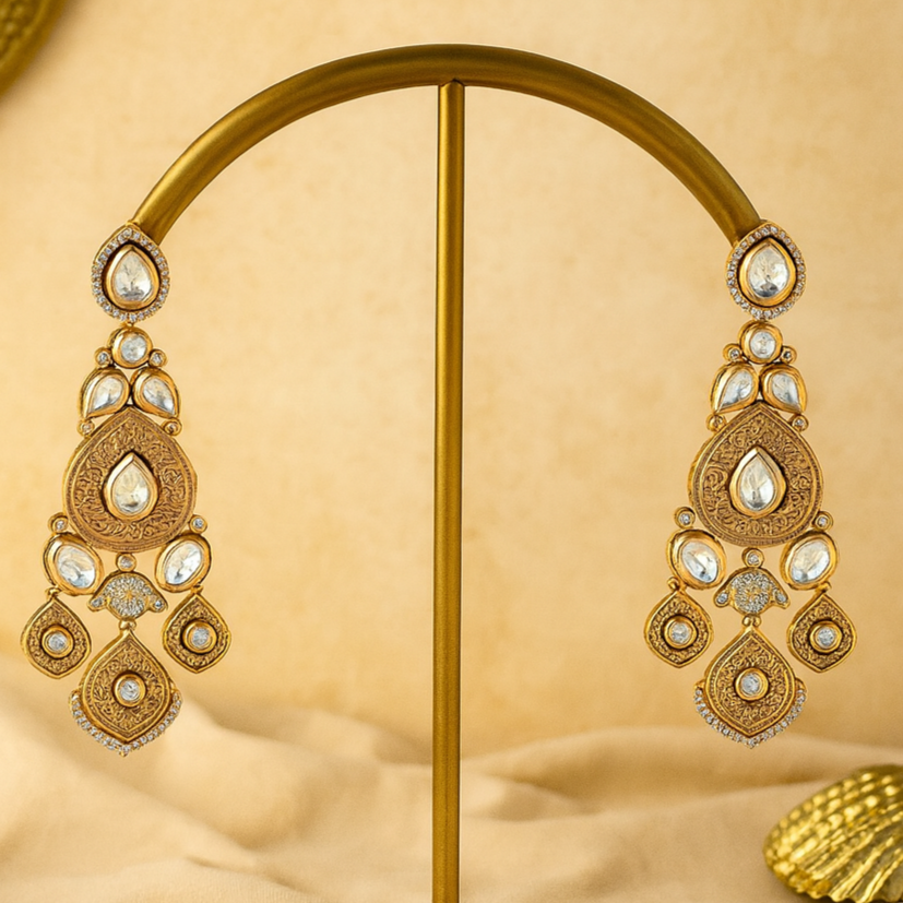 Ornate gold earrings on a matching stand against a beige background