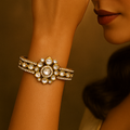Woman wearing gold jewelry including earrings and a bracelet against a warm-toned background