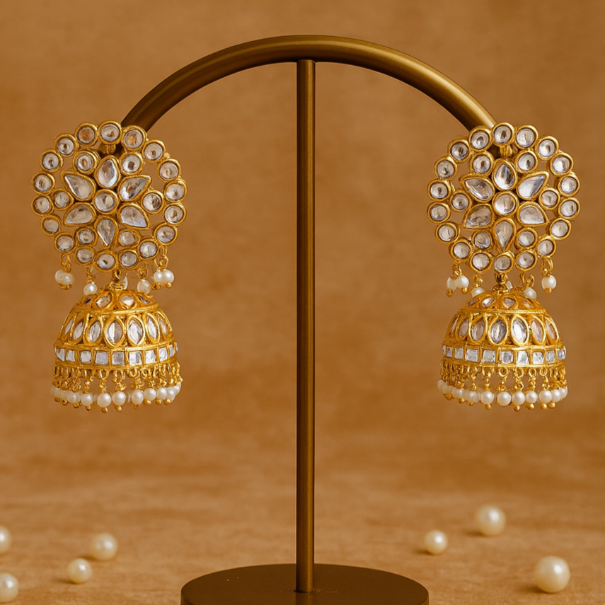 Gold and pearl earrings on a brown stand with scattered pearls on a brown background