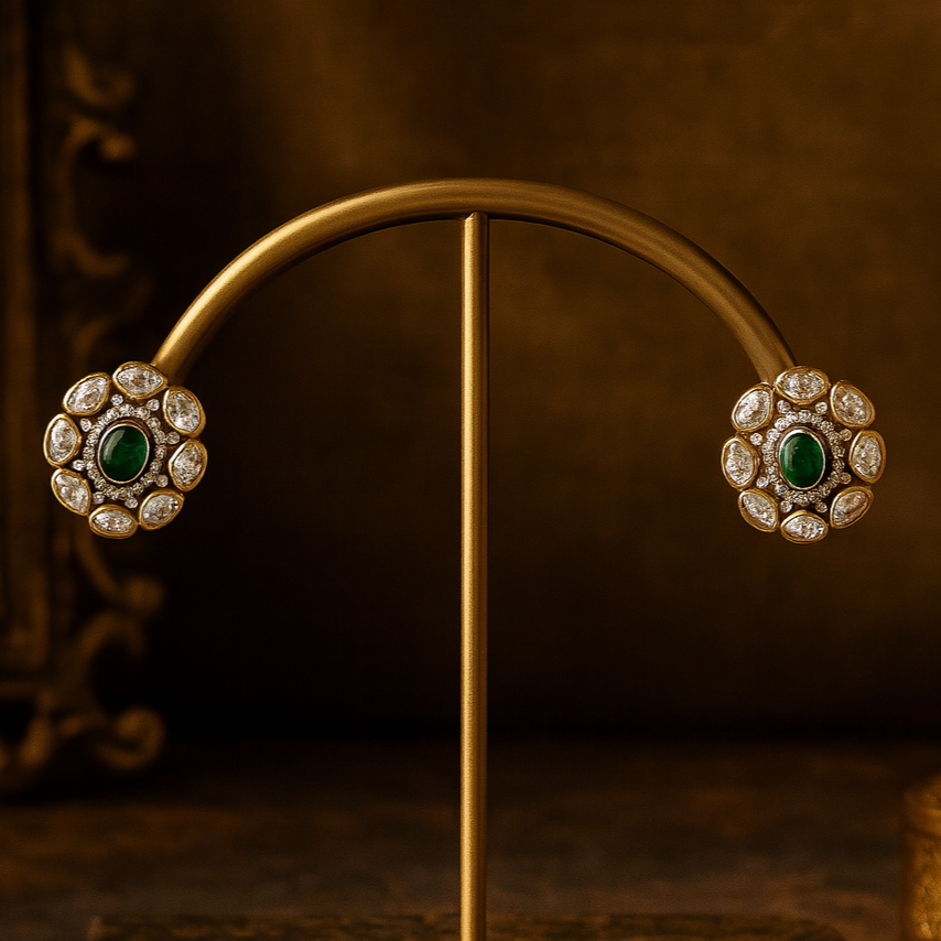 Pair of gold earrings with green gemstones on a stand against a dark background