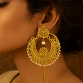Woman wearing a gold earring with intricate design against a warm brown background