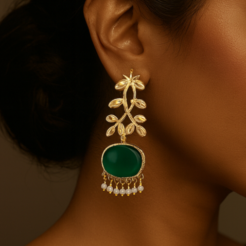 Woman wearing a gold earring with a green gemstone against a brown background