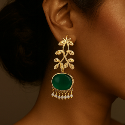 Woman wearing a gold earring with a green gemstone against a brown background