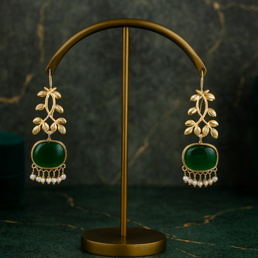 Gold earrings with green stones on a gold stand against a dark background