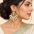 Model wearing a Kanika green chandbali earring with clear stones and cream pearl-style drops, paired with an ivory saree and sage border.