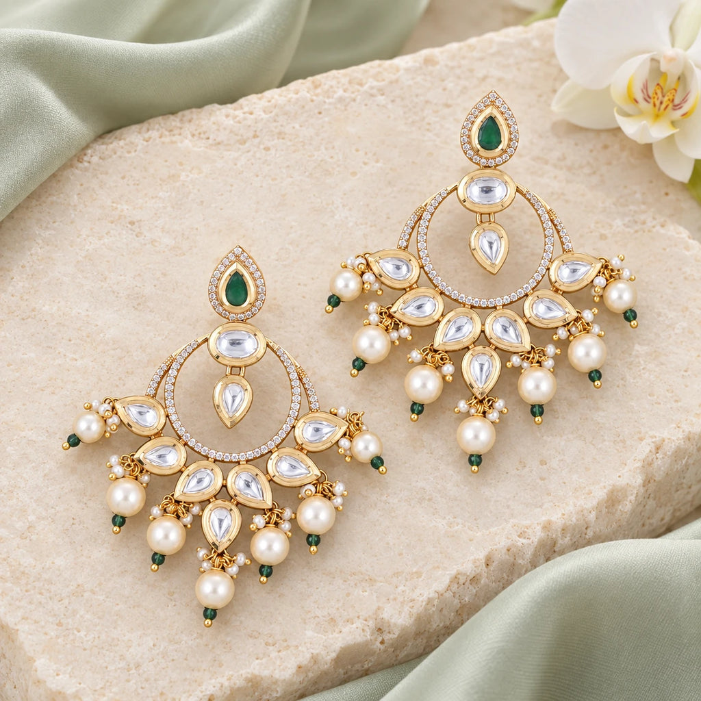 Pair of Kanika green and pearl-style chandbali earrings on cream stone beside pale sage silk and a white orchid.