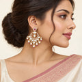 Indian model in an ivory saree with a dusty rose border wearing a Kanika ruby-colour chandbali earring with cream pearl-style drops.