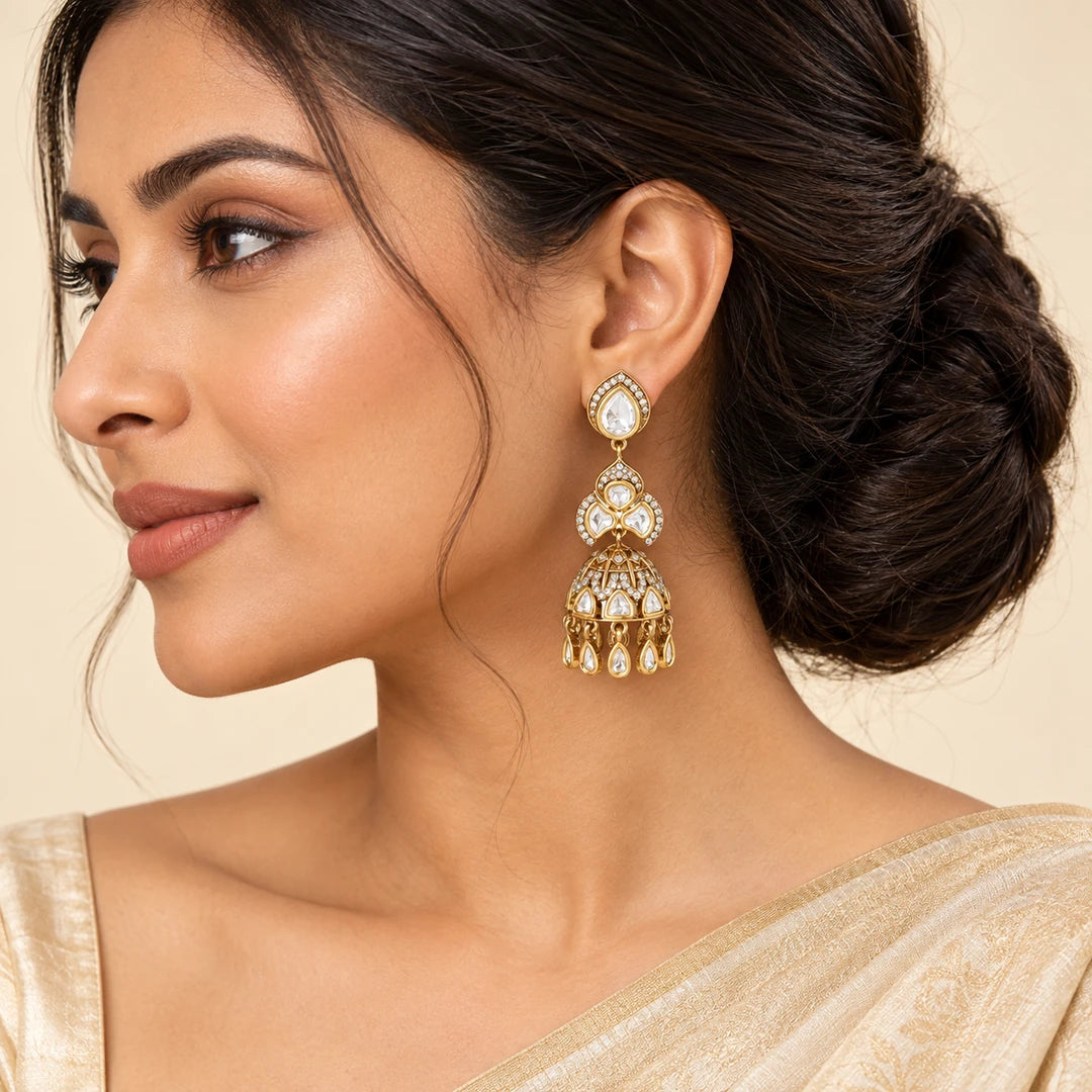 Indian model in an ivory and champagne saree wearing a vertically hanging Kashika clear and gold-tone jhumka earring.