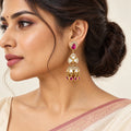 Indian model in an ivory saree with a rose border wearing a vertically hanging Kashika ruby-colour jhumka earring.