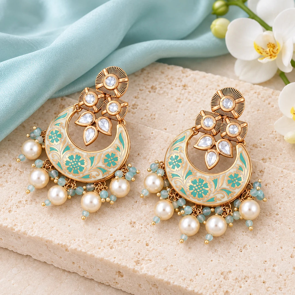 Pair of Kumud ivory and aqua floral chandbali earrings on cream stone beside pale aqua silk and a white orchid.