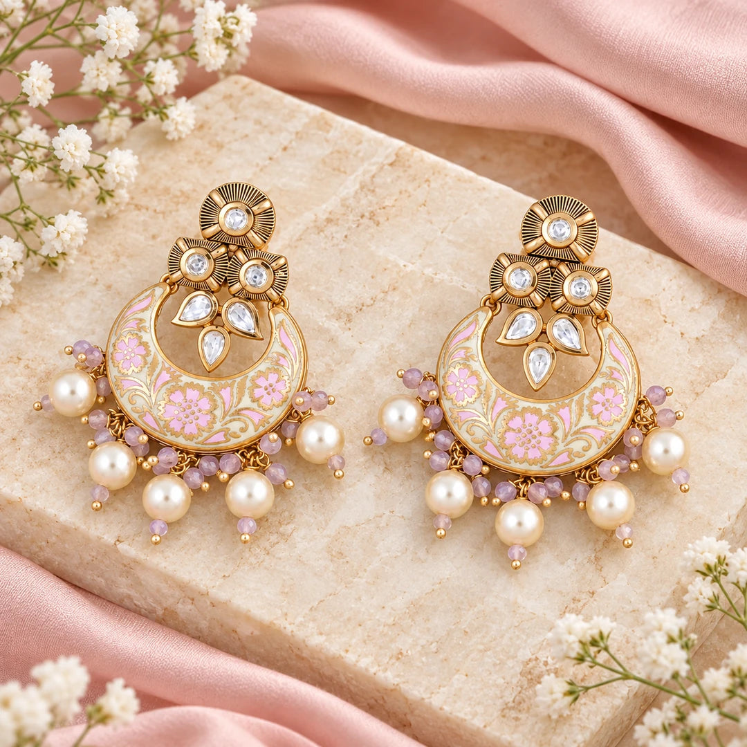 Pair of Kumud ivory and pink floral chandbali earrings with cream pearl-style drops on cream stone beside blush silk and small white flowers.