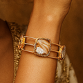 Woman wearing a gold bracelet against a warm brown background