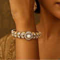 Woman wearing gold jewelry including earrings and a bracelet against a warm-toned background