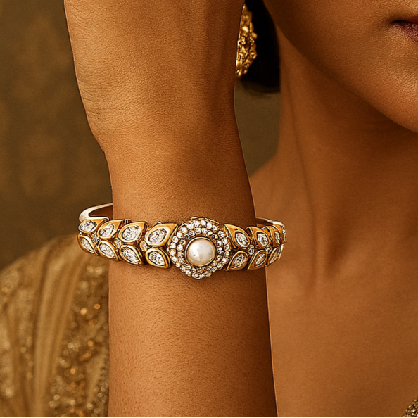 Woman wearing gold jewelry including earrings and a bracelet against a warm-toned background