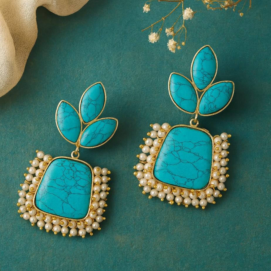 Turquoise earrings with gold and pearl accents on a teal background