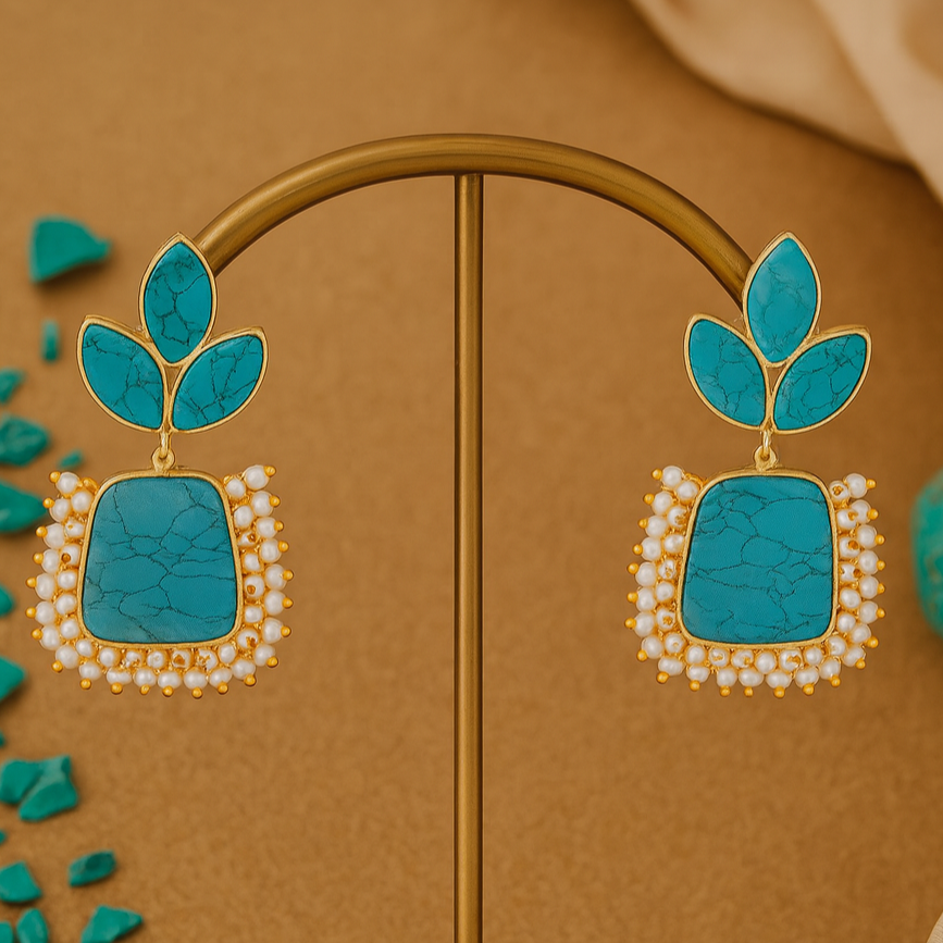 Pair of turquoise earrings with gold and pearl accents on a brown background.
