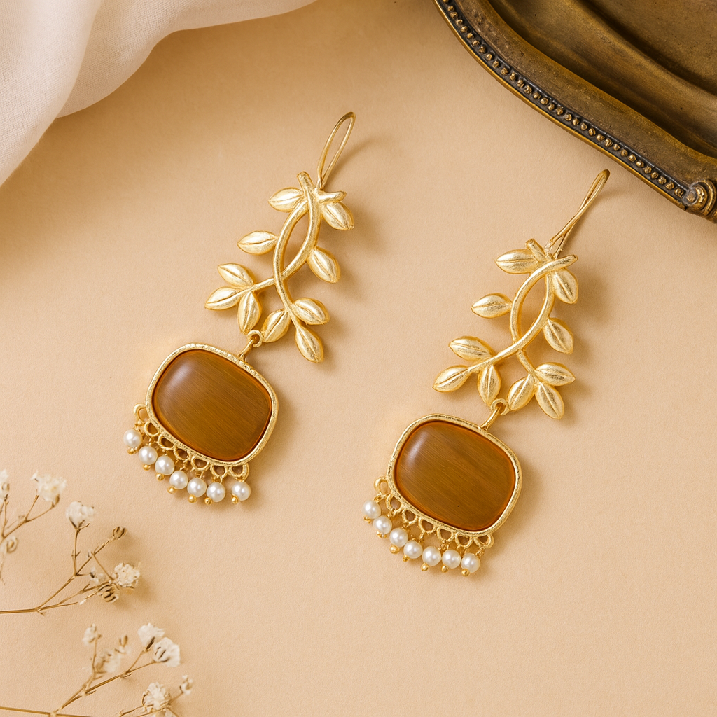 Gold earrings with brown stones and pearl accents on a beige background
