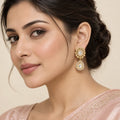 Model in a blush saree wearing Aabha gold-tone earrings with clear stone rosettes and teardrop pendants.