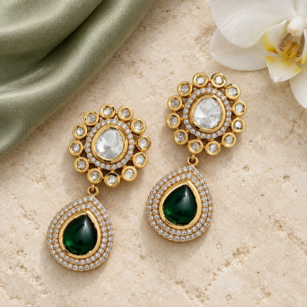 Aabha green teardrop earrings with clear-stone rosettes on cream stone beside sage silk and a white orchid.