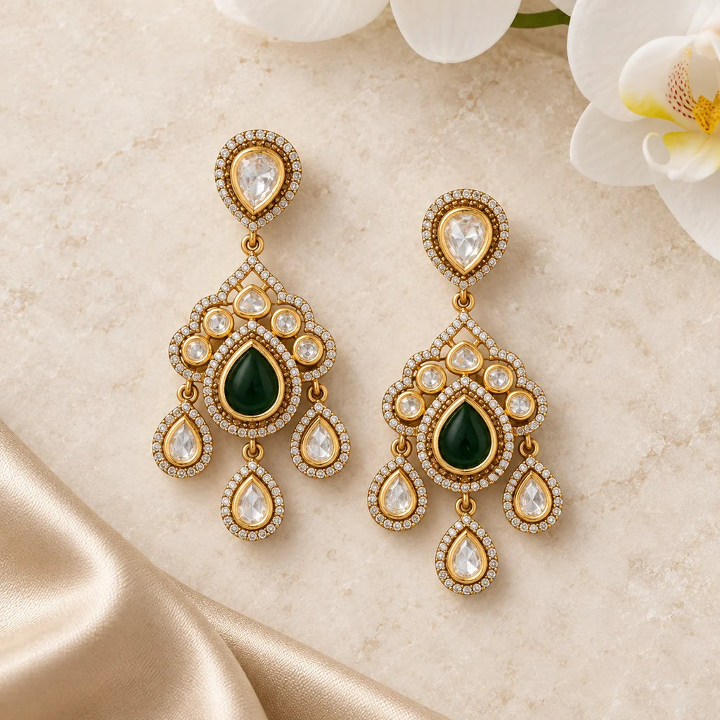 Pair of Advika green Kundan chandelier earrings on ivory stone beside champagne silk and a white orchid.