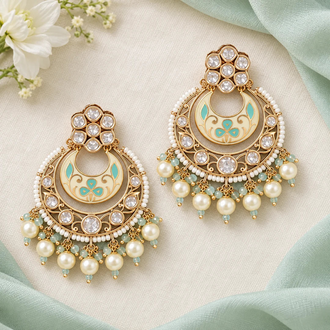 Pair of ivory and mint chandbali earrings lying flat on ivory fabric, framed by mint silk and white flowers.