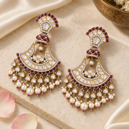 Pair of Chandrika wine chandbali earrings on a cream stone display with ivory silk, rose petals and a brass bowl.