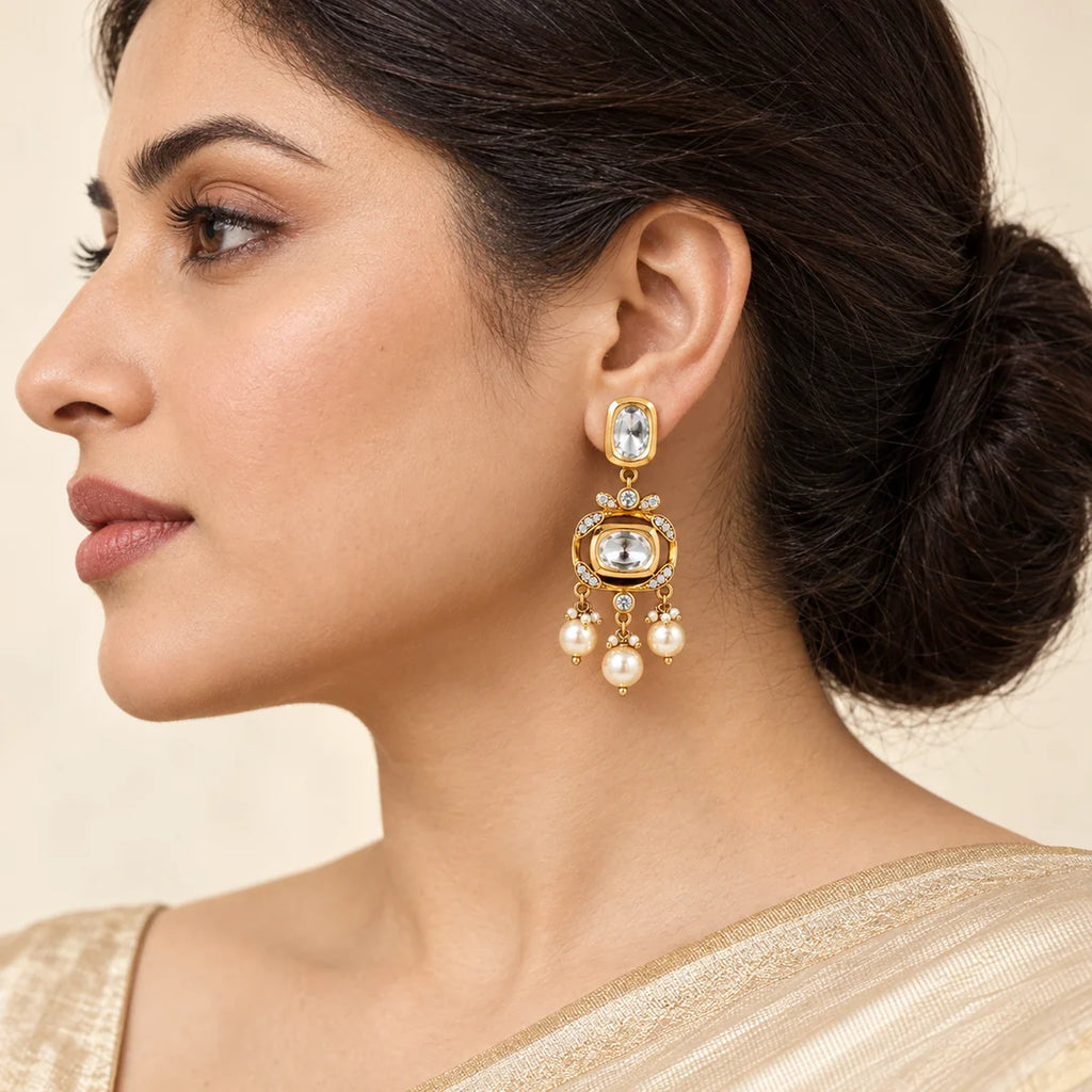 Side-profile Indian model wearing a Charvi gold-tone earring with clear stones and three cream pearl-style drops.