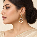 Side-profile Indian model wearing a Charvi gold-tone earring with clear stones and three cream pearl-style drops.