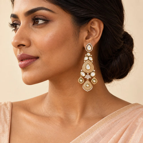Indian model in a peach saree wearing a long antique gold-tone chandelier earring with clear stones and three engraved drops.