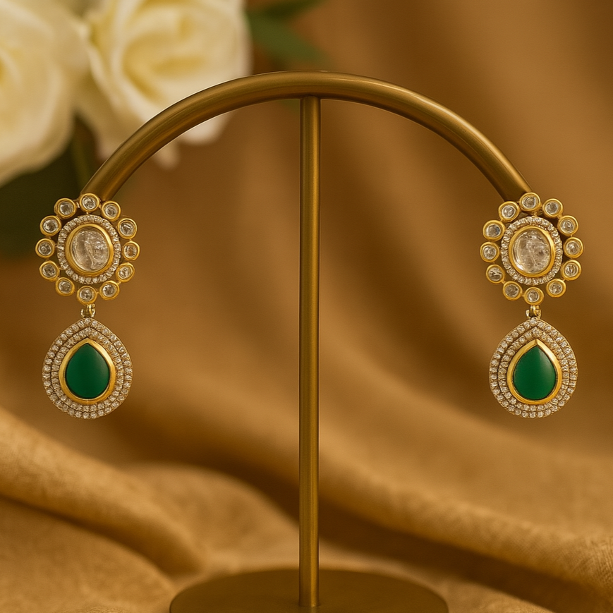 Gold earrings with green gemstones on a gold stand against a brown fabric background