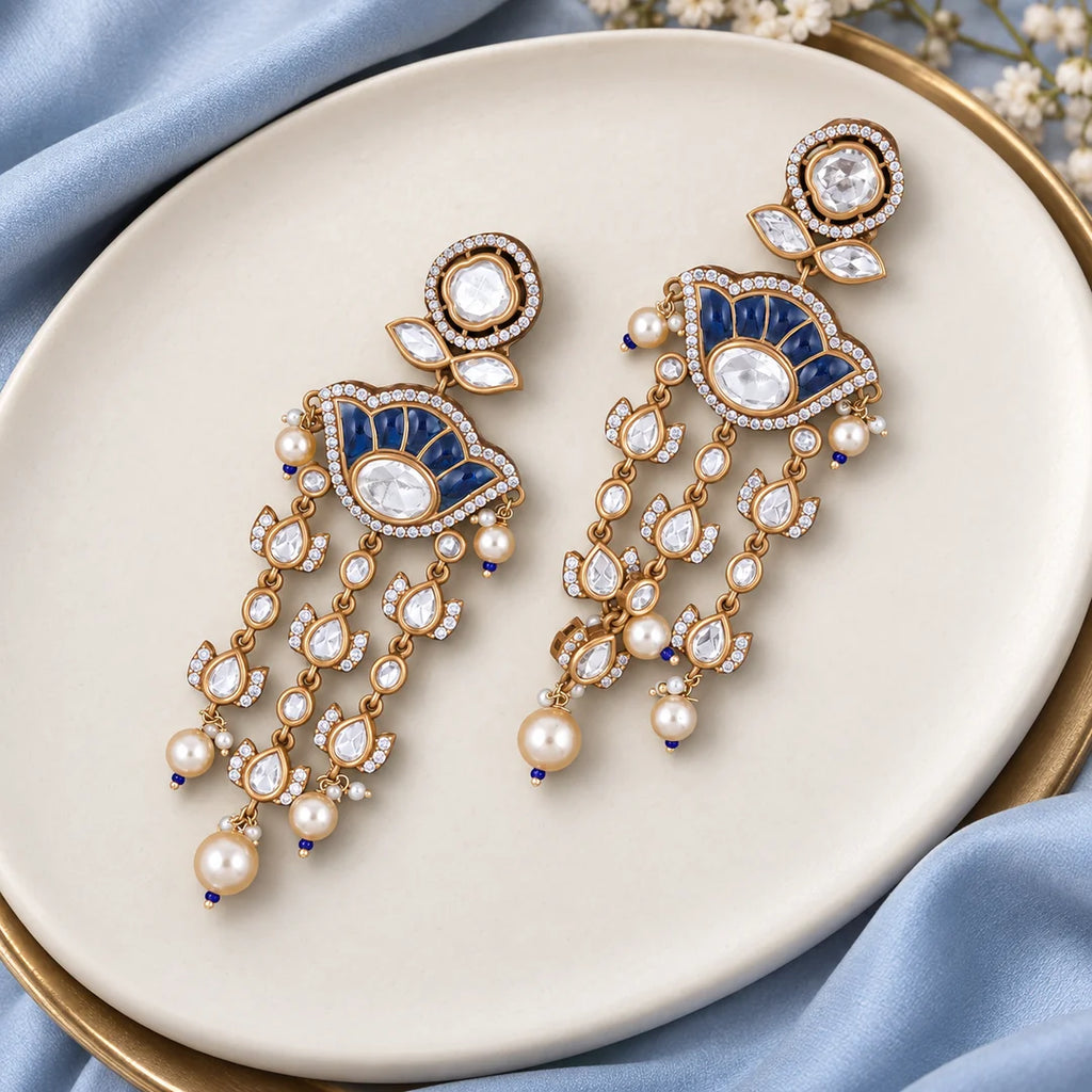 Pair of Gulika blue chandelier earrings on an ivory display with pale-blue silk and delicate floral props.