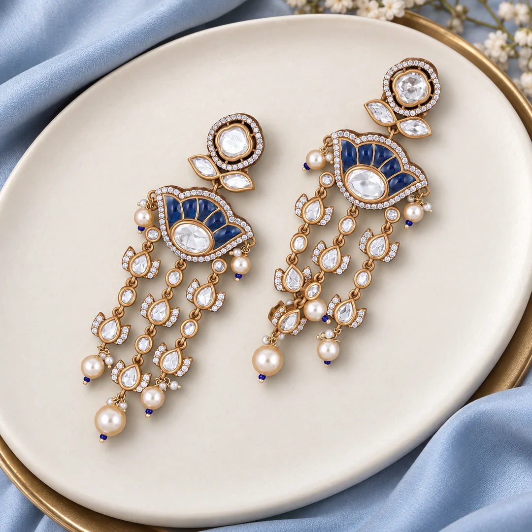 Pair of Gulika blue chandelier earrings on an ivory display with pale-blue silk and delicate floral props.