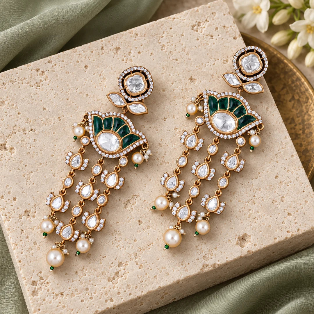 Pair of Gulika green chandelier earrings on an ivory stone display with sage silk and white floral props.