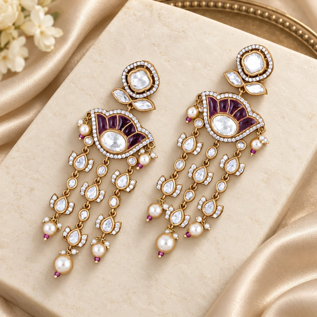 Gulika wine chandelier earrings with clear stones and pearl-look drops on an ivory display with champagne silk.