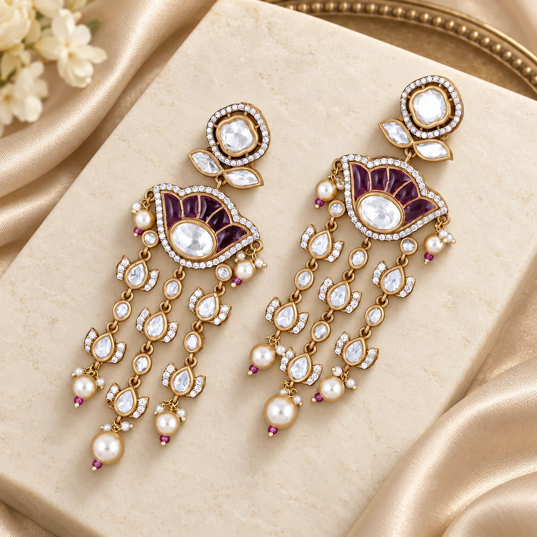 Gulika wine chandelier earrings with clear stones and pearl-look drops on an ivory display with champagne silk.