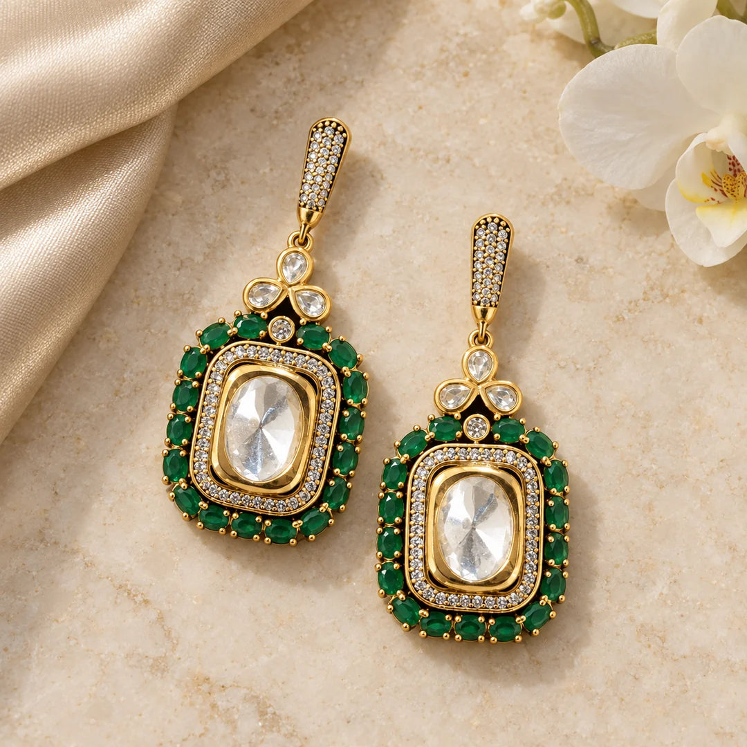 Pair of Harita green rectangular drop earrings on cream stone beside champagne silk and white orchids.